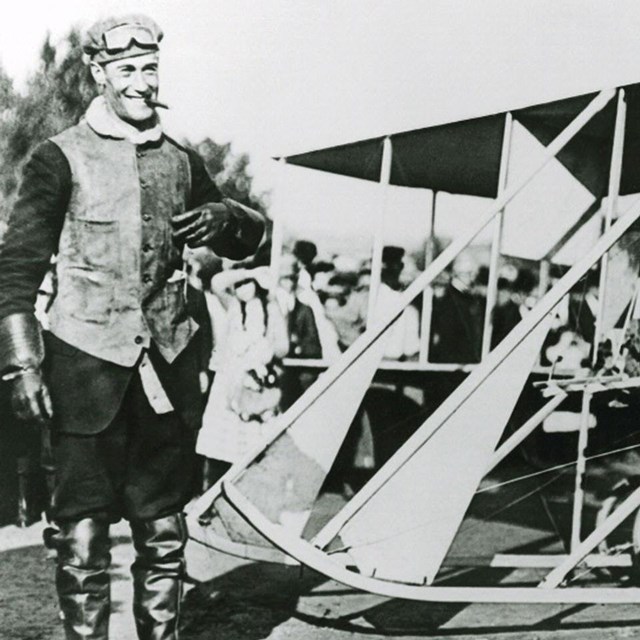 A man standing next to an early model airplane