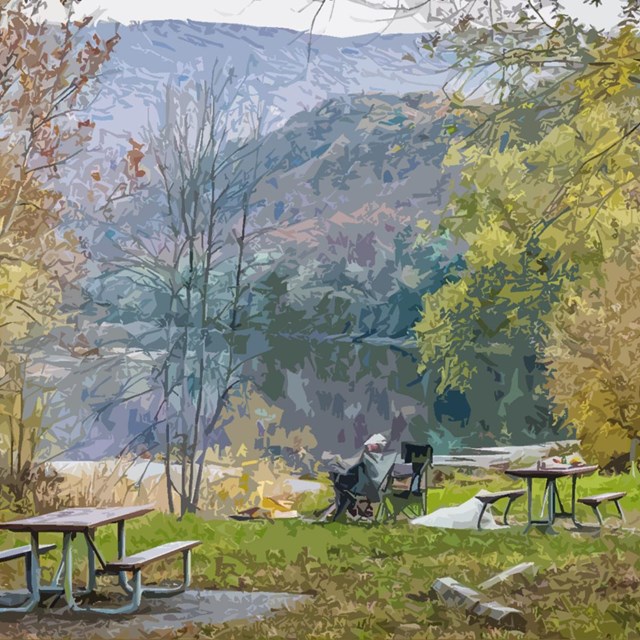 A man sits in a chair looking out over fall colors on the water.