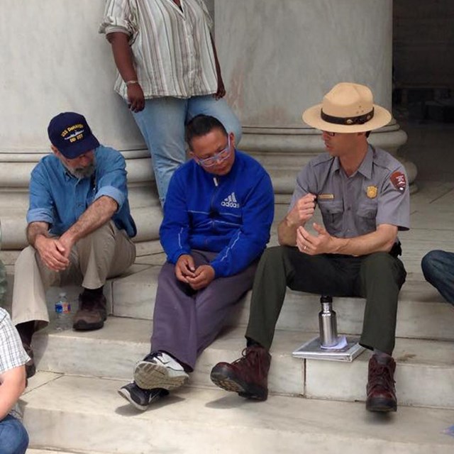 Park ranger chats with people while sitting on steps.