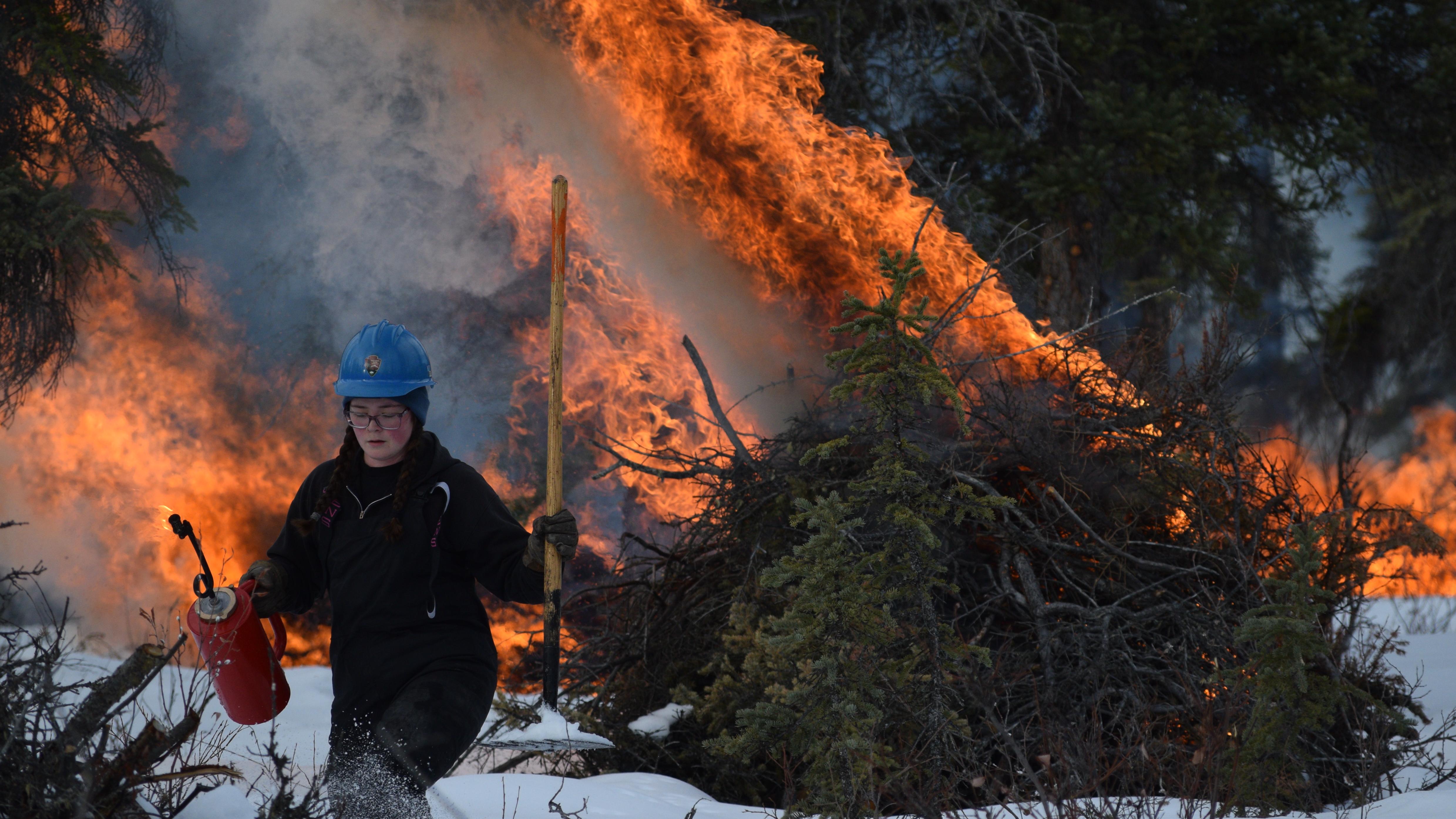 A firefighter with a pile burning behind them