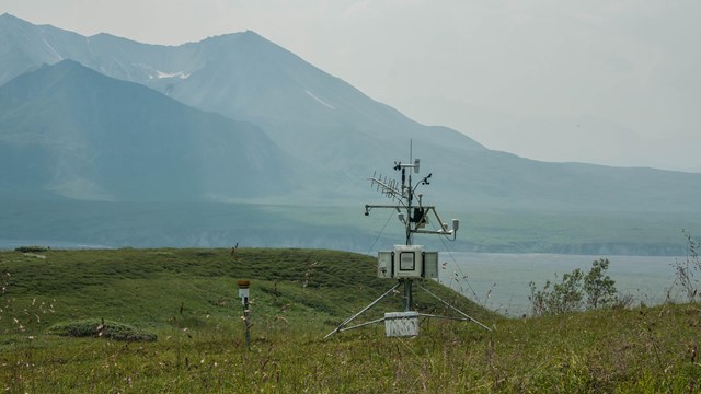 Weather monitoring equipment on a tundra hillside, with hazy mountains in the distance.