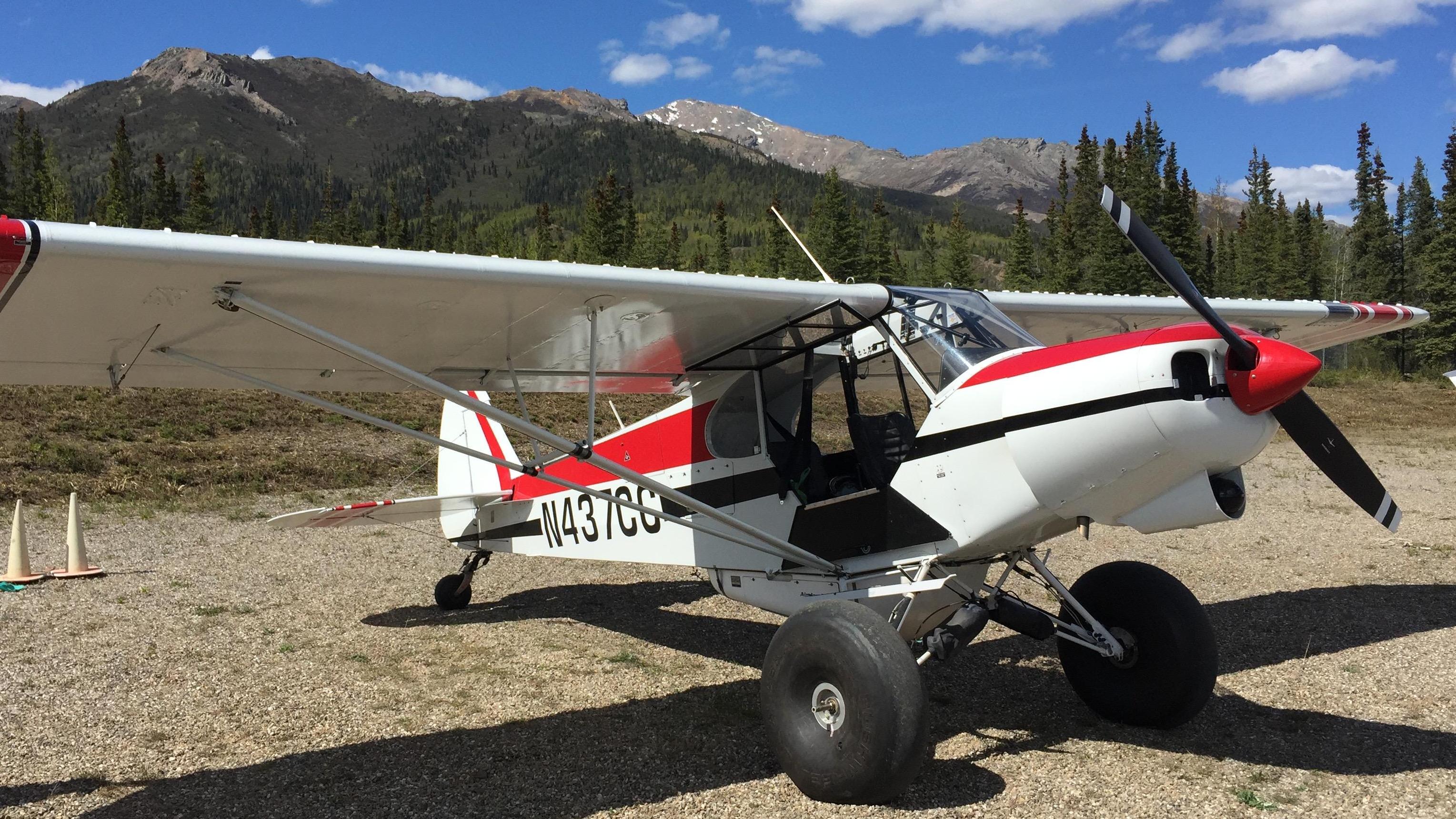 A small, red and white, two seater, propeller plane parked on a gravel strip.