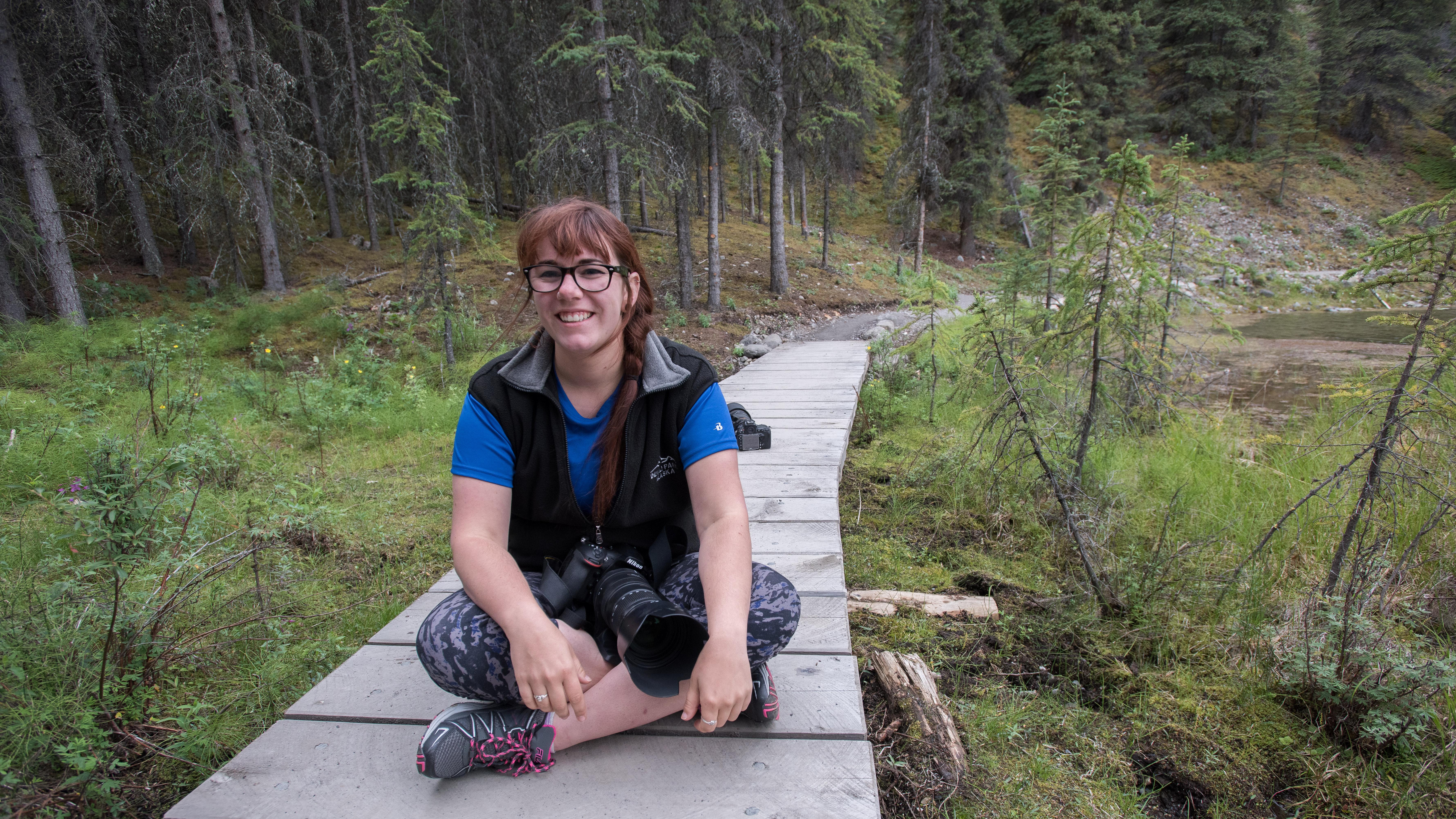 a young woman sitting on a boardwalk in a forest