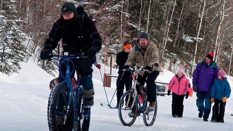 several people riding fat tire bikes while others walk on a snowy road