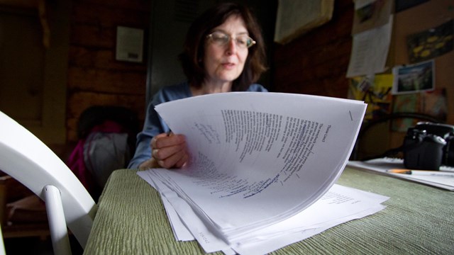 a woman shifts through a stack of papers on a desk