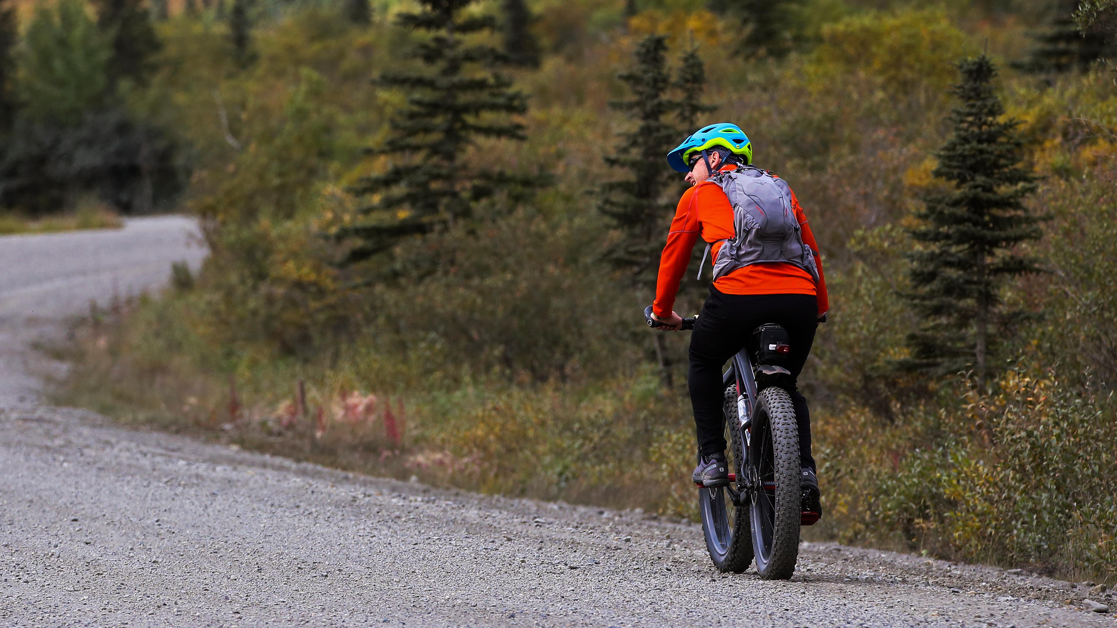 A cyclist travels along a gravel road wearing a bright red shirt and blue/green helmet.