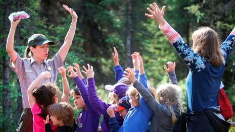 A ranger and kids stand with their arms in the air, making animal claws with their hands.