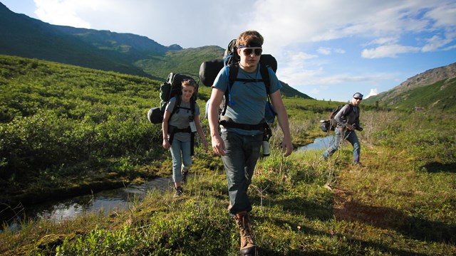 three people hiking through a small creek on a hill