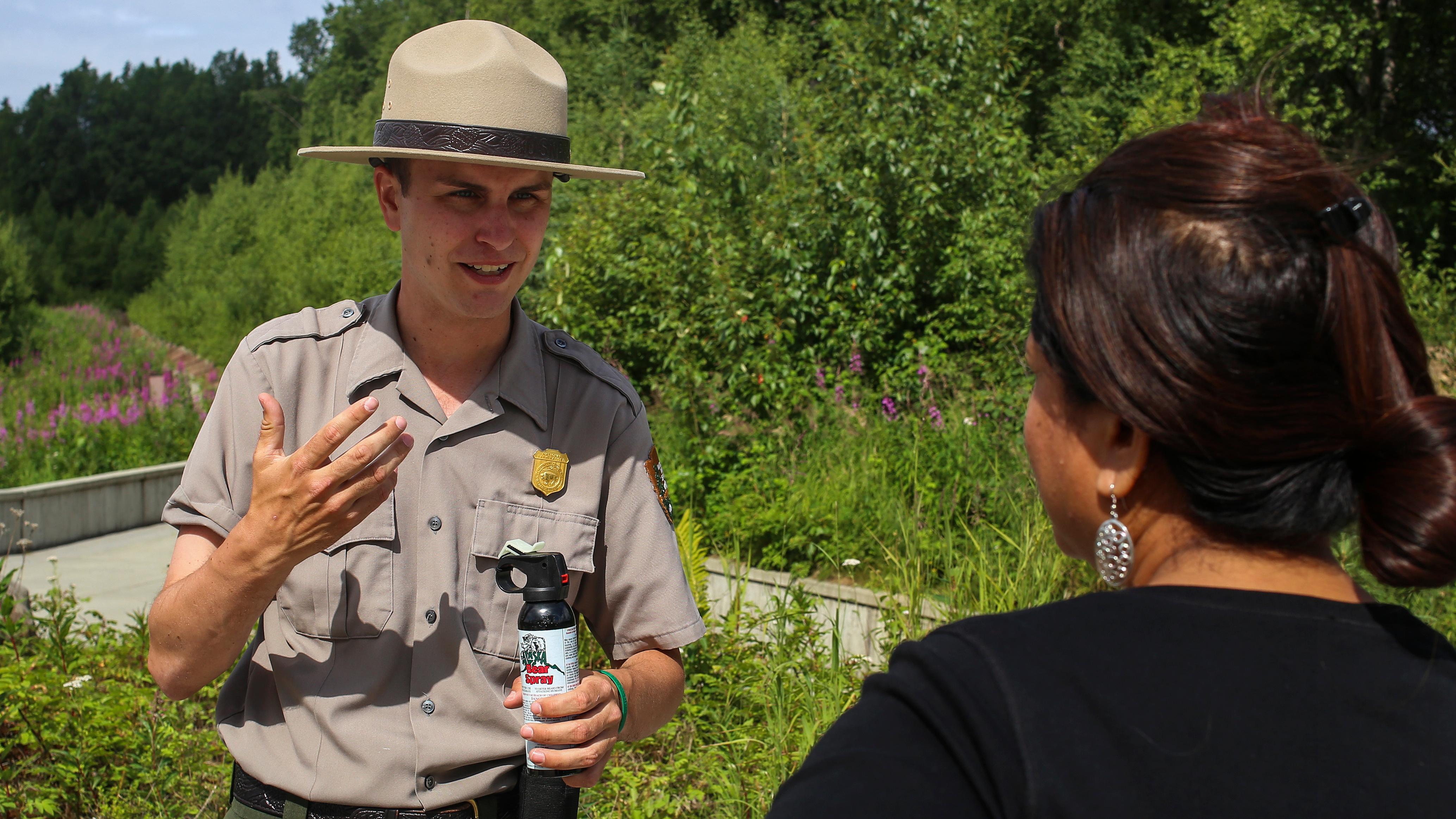 A park ranger holds a can of bear spray and talks to a woman.