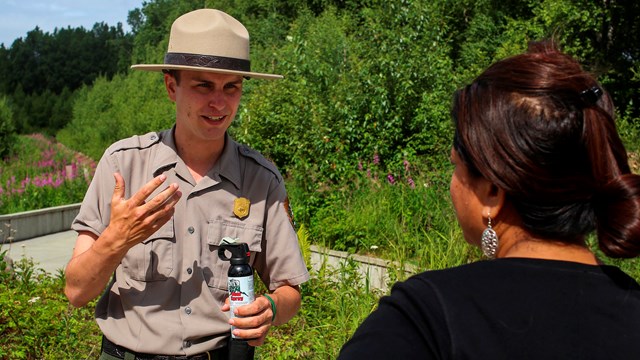 A park ranger holds a can of bear spray and talks to a woman.