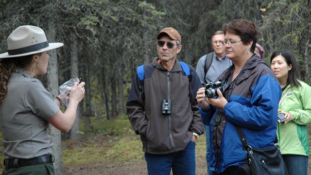 a female ranger shows a group of people an object on a trail