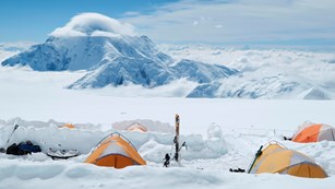 snowy, mountainous landscape with numerous people and tents in the distance