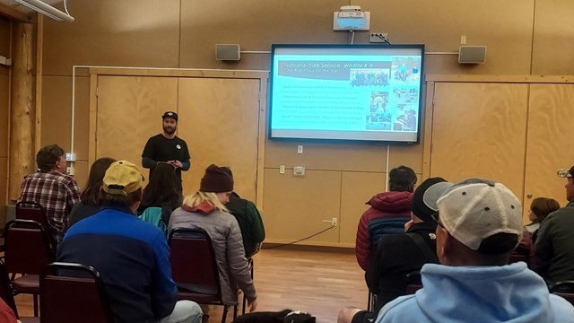 A speaker presents a powerpoint presentation to a crowd.