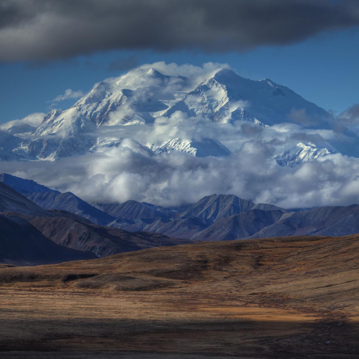 a tall snow-capped mountain peaking out of the clouds