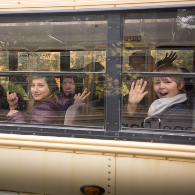 children wave from a bus window