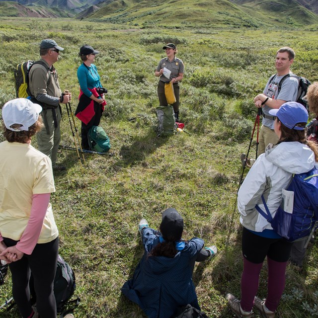 woman in ranger uniform and four others hiking through a meadow