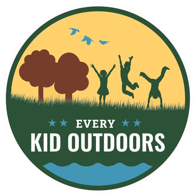Every Kid Outdoors program logo. Cartoon children play in the grass next to two trees.