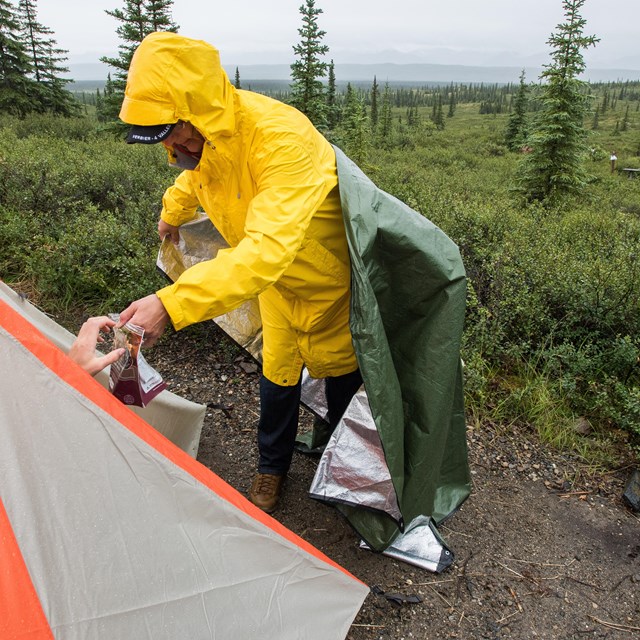 person in rain gear setting up a tent