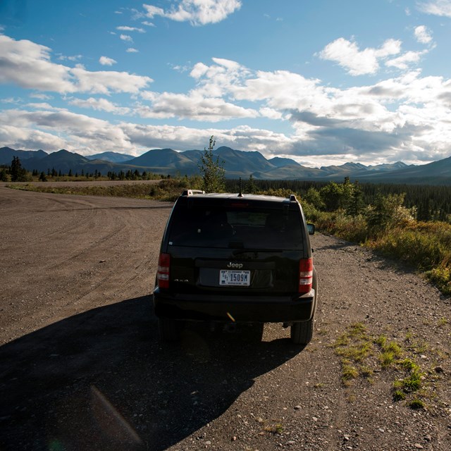 an SUV parked on the shoulder of a dirt road 