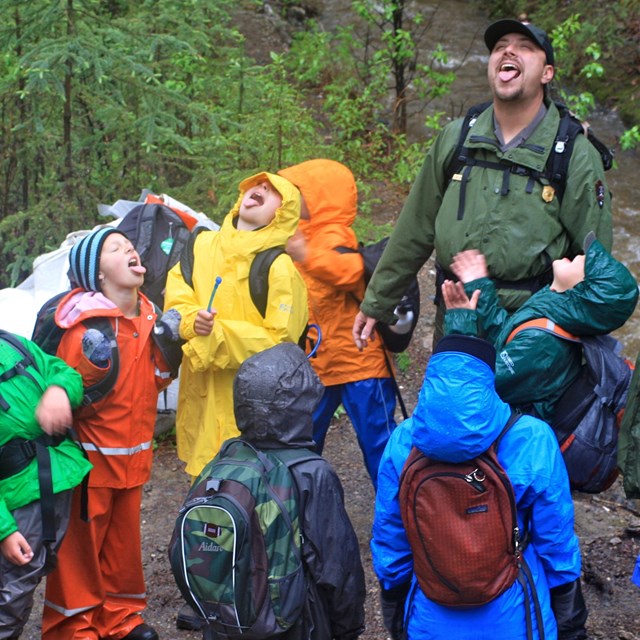 A group of students and rangers turn their faces skyward to taste the rain