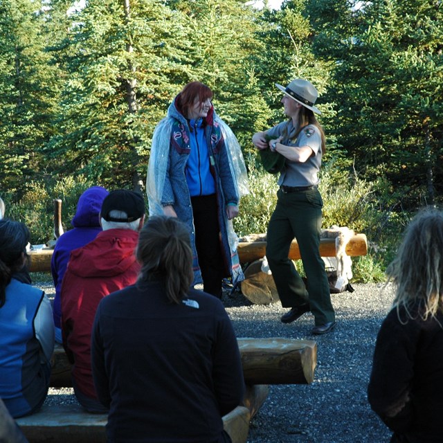 a female ranger speaking to a group of people seated around her in a forest clearing