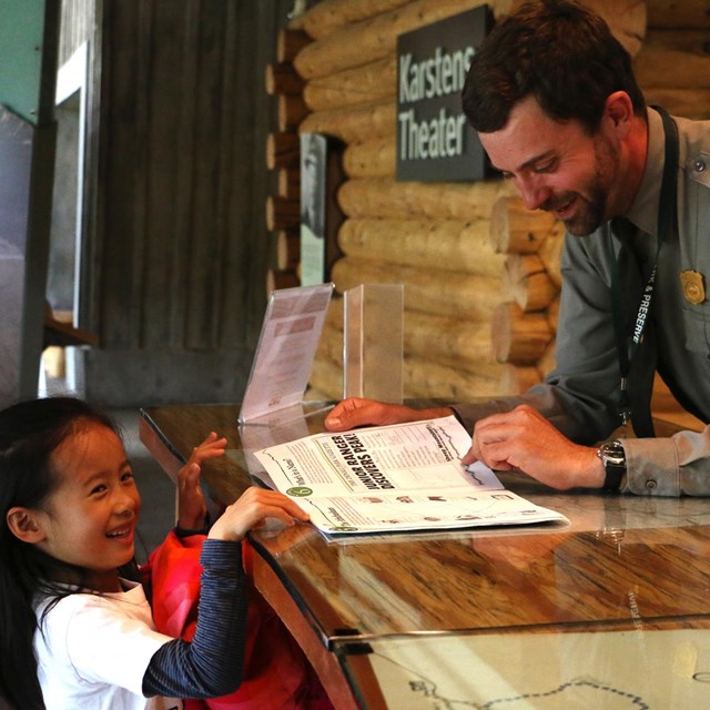 a girl smiles as a park ranger checks her junior ranger book