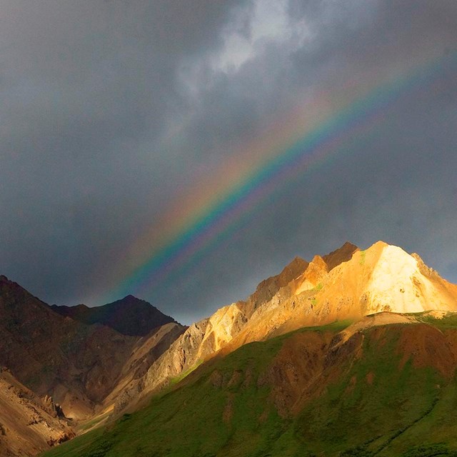 a rainbow shines behind a rocky ridge