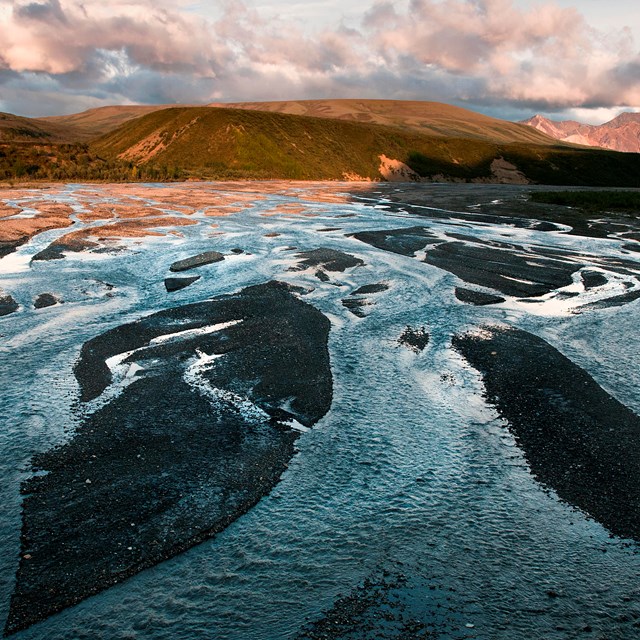 A braided river with channels of water and gravel bars stretches into the distance toward mountains.