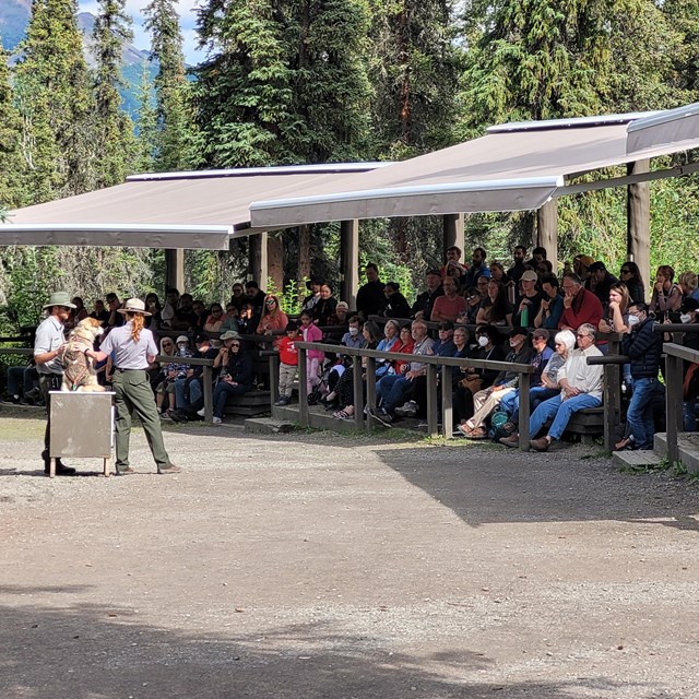 Two rangers stand with a dog in front of a crowd