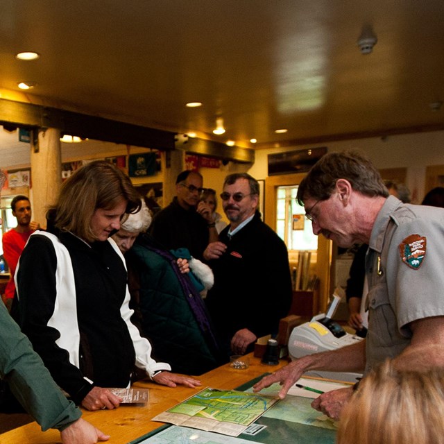 a woman in a ranger uniform sitting at a computer, talking to visitors