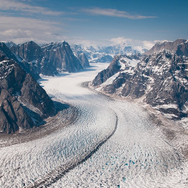 aerial view of a massive glacier flowing out of craggy mountains