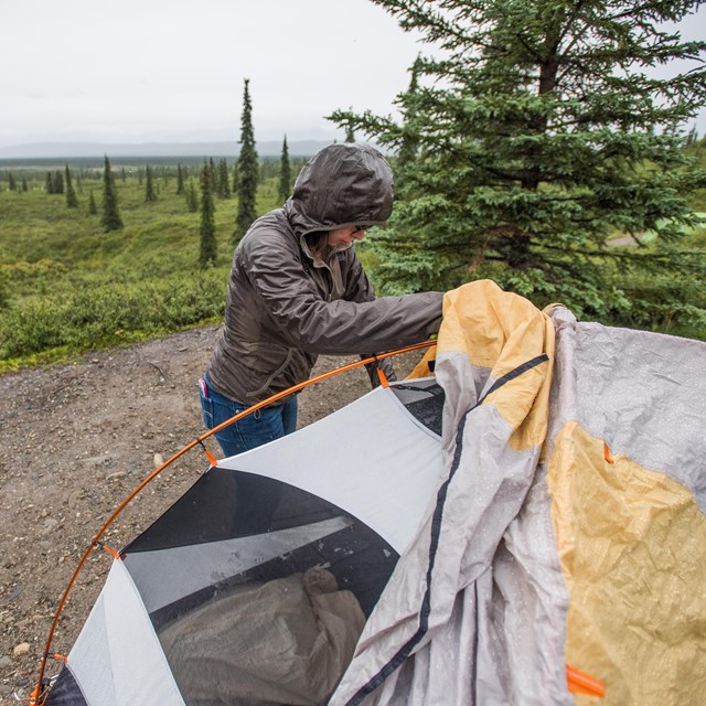 person in rain gear setting up a tent