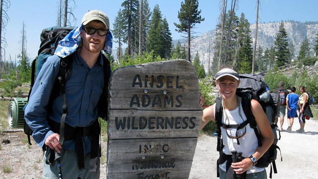 Wilderness backpackers pose near Ansel Adams Wilderness sign.