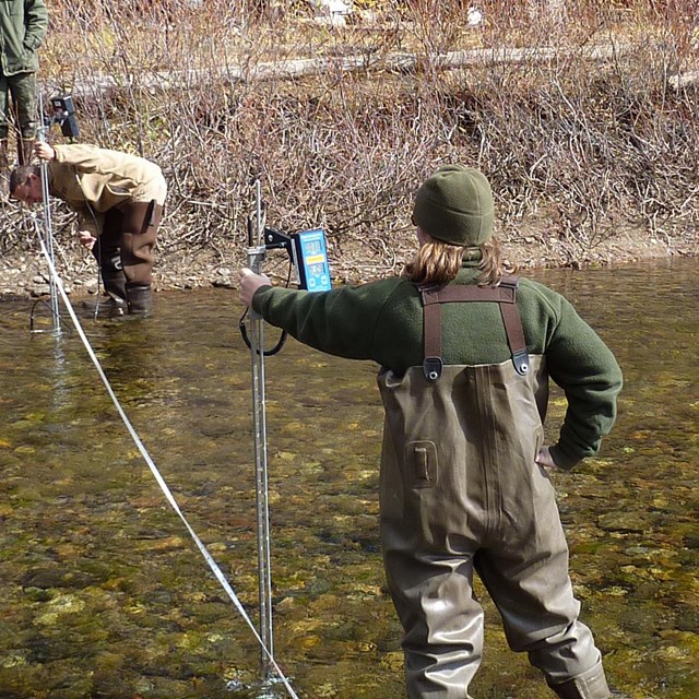 Two scientists stand in river taking measurements that will help them estimate river discharge.