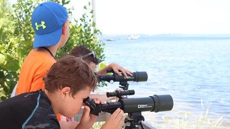 Two Junior Ranger look out of telescopes over the water