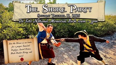 Two reenactors dressed as pirates sword fighting on a beach