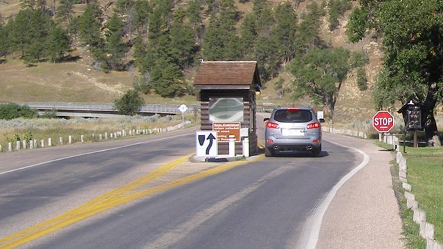 Car at park entrance station with NPS arrowhead sign in foreground and Tower in background