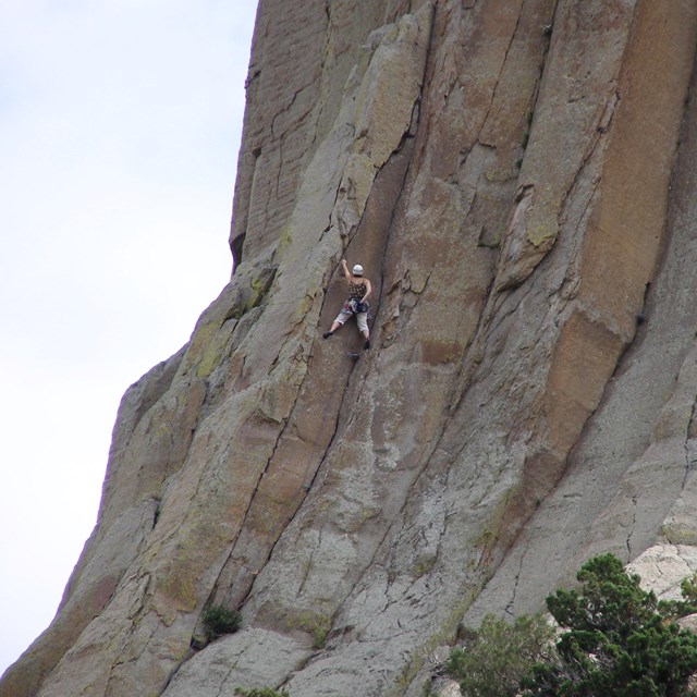 A woman reaches for chalk as she climbs Devils Tower