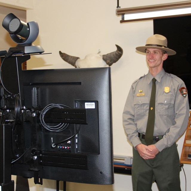 A ranger standing in front of teleconferencing equipment.