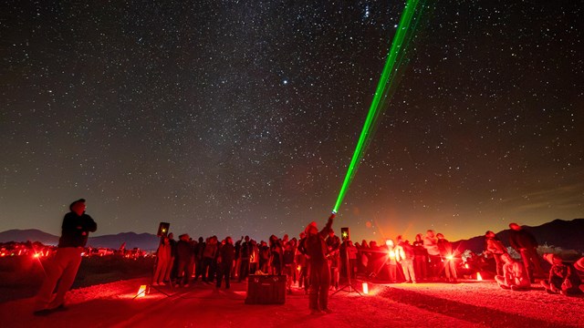 The photograph captures a night sky filled with stars above a group of people engaged.