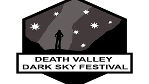Death Valley Dark Sky logo with a person standing looking at a star-filled sky.