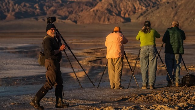four people taking pictures of mountains and salt flats as a man smiles at the camera
