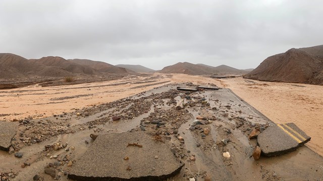 Large pieces of asphalt in road with large flows of brown water coming from mountain landscape.