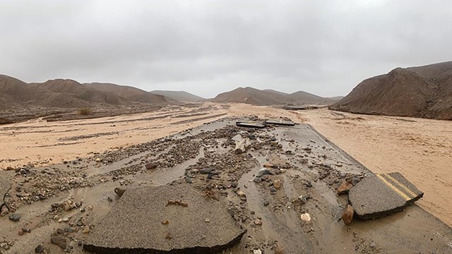 Damaged pavement with brown streams of water washing down a canyon.