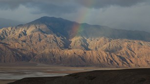 A rainbow reaches down to shimmering desert mountains.