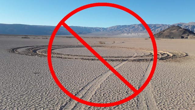 Tire tracks scar a smooth desert playa, red circle with line through it on top