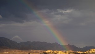 a rainbow touches eroded yellow hills with a dark, stormy background