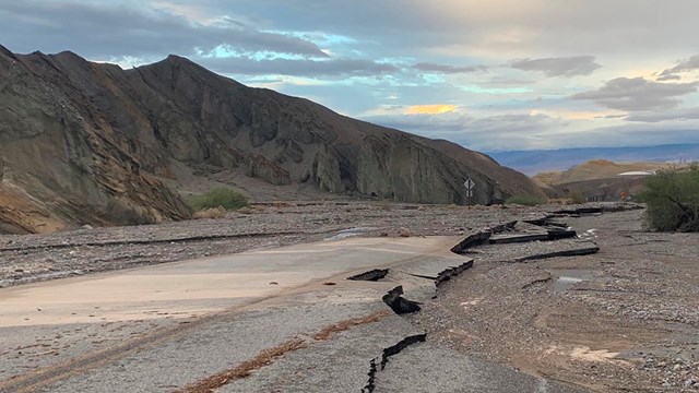 Pavement is broken with mud and debris across the road surrounded by mountains.