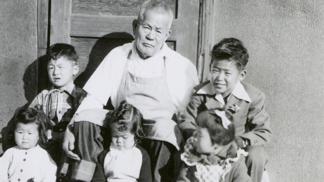 Six people sitting on steps of a building with a wooden door in the background.