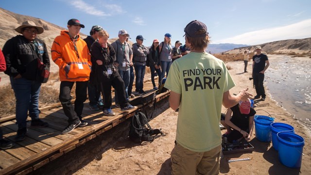 Volunteers stand along a boardwalk facing an employee giving directions. 